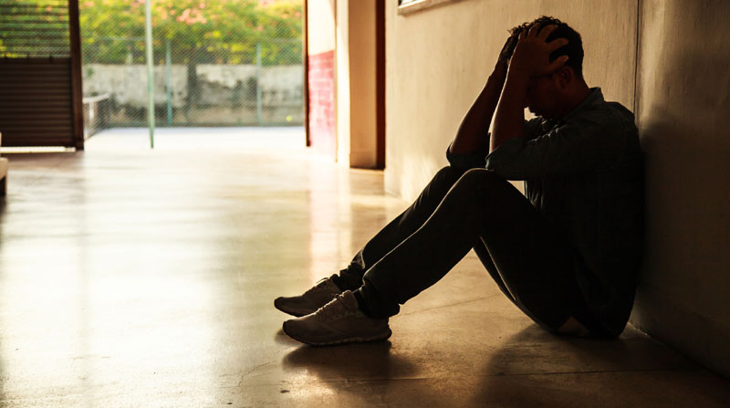 Young man sitting on floor looking dejected.