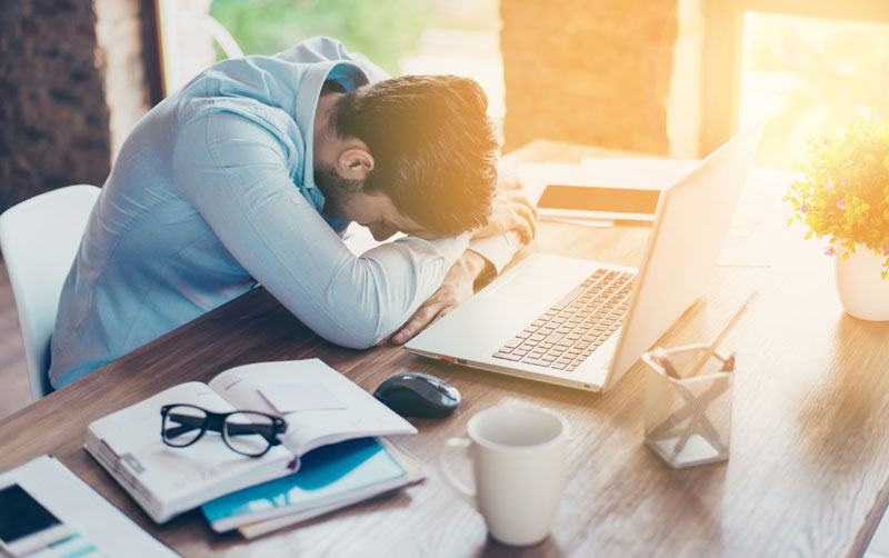 Man sleeping at his desk with laptop and papers around.